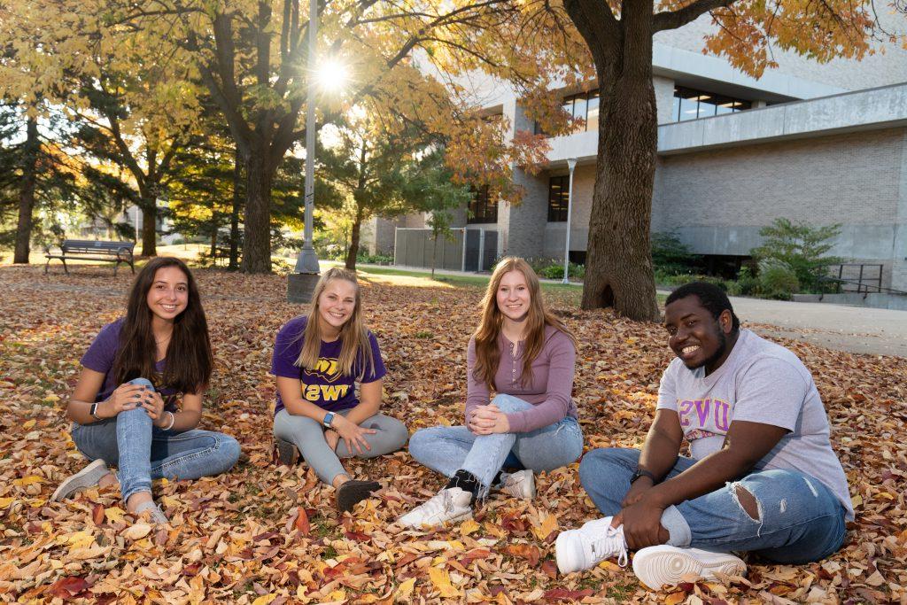 Student admissions ambassadors sitting in the fall leaves next to Albertson Hall.